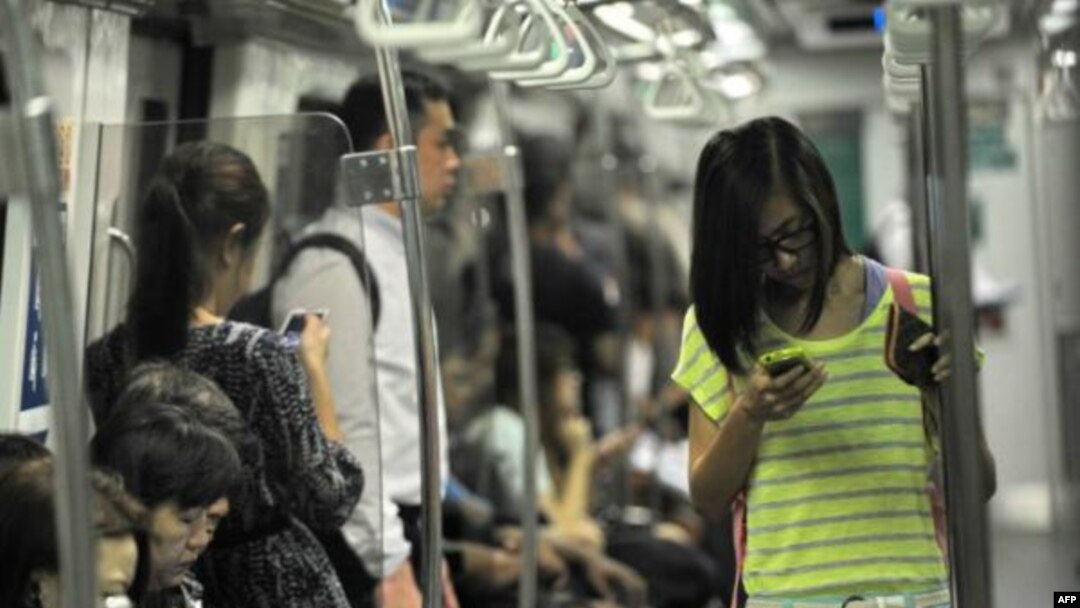 Penumpang kereta bawah tanah di Singapura asyik dengan ponsel pintar mereka (30/4). (AFP / Roslan Rahman)