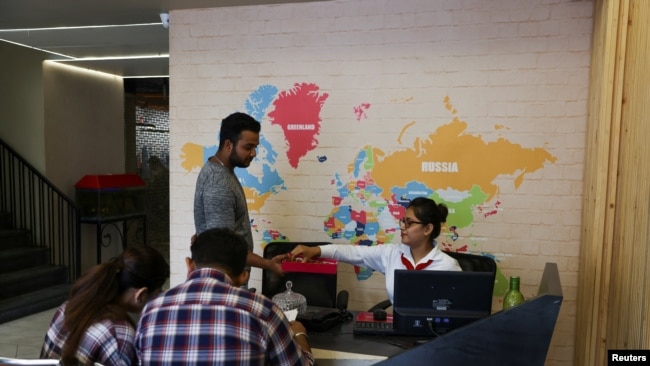 Sachin, 19, offers sweets to the receptionist at Western Overseas, an institute providing coaching for English language proficiency tests and visa consultancy, after his visa was approved, in Ambala, India, August 4, 2022. REUTERS/Anushree Fadnavis