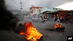 FILE - Police drive past burning tires lit by anti-government protestors, in Port-au-Prince, Haiti, Oct. 4, 2019. 