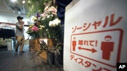 Shinichiro Hirano berjalan di tokonya, Sun Flower Shop, di mana dia memasang peringatan agar pelanggan menjaga jarak aman, di tengah pandemi virus corona, 22 Juni 2020, di Tokyo. (Foto: AP)