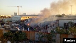 Smoke raise as people check the damaged after a rocket hit a camp for displaced people during the fight between rival armed groups in Tripoli, Libya, Sept. 2, 2018. 