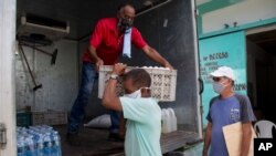 FILE - Cafeteria owner Miguel Sanchez, right, inspects his purchase porters load into a courier service's truck, to take to his restaurant in Havana, Cuba, July 31, 2020, as government is letting private businesses buy wholesale for the first time.