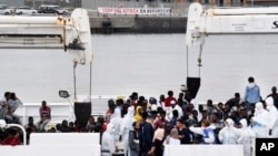 Para aktivis membentangkan spanduk bertuliskan imbauan untuk menghentikan serangan terhadap para pengungsi, saat para migran tengah menunggu untuk turun dari kapal penjaga pantai Italia "Diciotti" saat berlabuh di pelabuhan Sisilia, Catania, Italia selatan, Rabu, 13 Juni 2018. (Foto: dok).