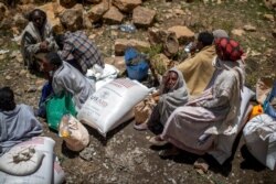 FILE - An elderly Ethiopian woman sits next to a sack of wheat given to her by the Relief Society of Tigray in the town of Agula, in the Tigray region of northern Ethiopia, May 8, 2021.