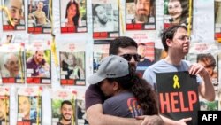 FILE— A couple embrace before posters of Israeli hostages held in Gaza since the October 7 attacks by Palestinian militants, during a protest by the families of the hostages and their supporters outside the Defence Ministry headquarters in Tel Aviv on April 25, 2024.