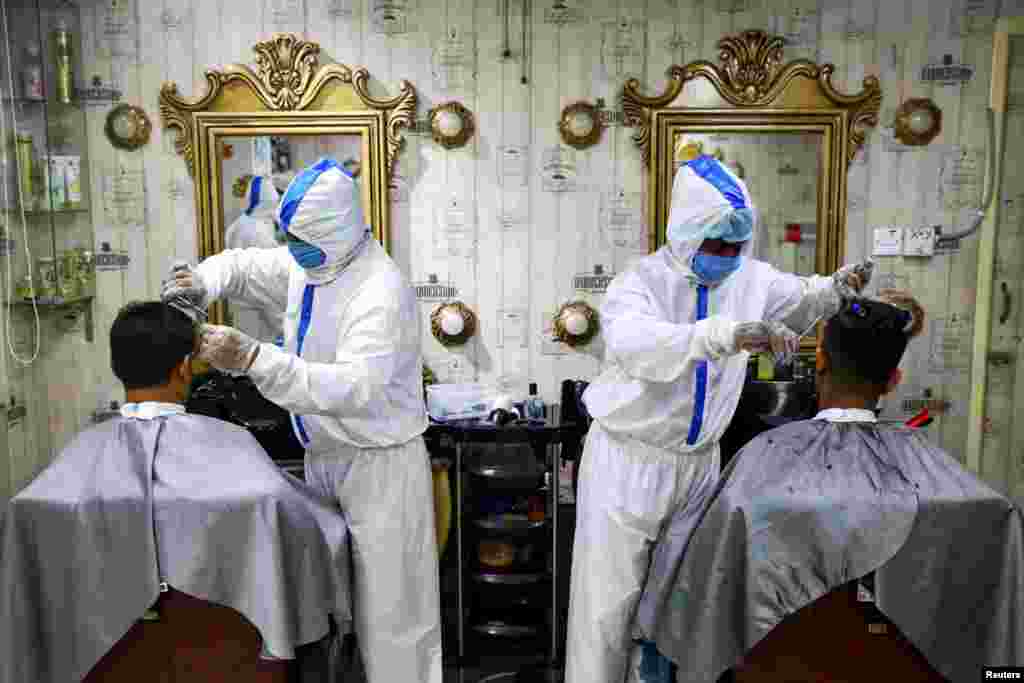 Barbers wearing protective suits and face masks provide hair cut service to the customers inside a salon in Dhaka, Bangladesh.