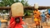 FILE - Women carry containers of water at a camp for internally displaced persons in Al Geneina, capital of West Darfur, Sudan, June 29, 2011. 