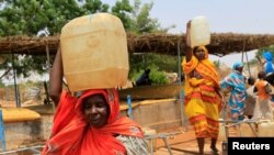 FILE - Women carry containers of water at a camp for internally displaced persons in Al Geneina, capital of West Darfur, Sudan, June 29, 2011. 