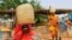 FILE - Women carry containers of water at a camp for internally displaced persons in Al Geneina, capital of West Darfur, Sudan, June 29, 2011. 