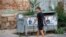 A pedestrian walks past garbage containers with election posters in the town of Kjustendil, Bulgaria, on July 9, 2021.