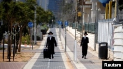 Pria Ultra-Ortodoks Yahudi mengenakan masker, berjalan di trotoar saat diberlakukannya lockdown di tengah meningkatnya kasus Covid-19 di Ashdod, Israel, 24 September 2020. (REUTERS / Amir Cohen)