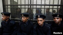 FILE - Some of the 14 Egyptian activists who were accused of working for unlicensed non-governmental organizations (NGOs) and receiving illegal foreign funds, stand in a cage during the opening of their trial in Cairo, Feb. 26, 2012.