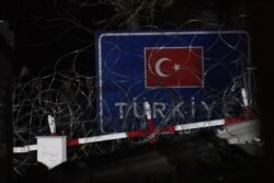 This picture taken from the Greek side of the Greece-Turkey border near Kastanies shows migrants standing behind razor wire, Feb. 29, 2020.