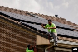 Workers install solar planers on the roof of a house in Rivas Vaciamadrid, Spain, Thursday, Sept. 15, 2022. The energy crisis is accelerating the installation of solar panels by residential communities in Spain who want to become self-sufficient. Recent legislation has allowed so-called "energy communities" to generate renewable power through collective installations. (AP Photo/Manu Fernandez)