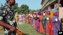 Indian security personnel guard as women voters stand in a queue to cast their votes at a polling station during the first of the five phase voting for state legislative assembly at Mahmoodpur village, in Samastipur district of India’s eastern state Bihar, Oct. 12, 2015.