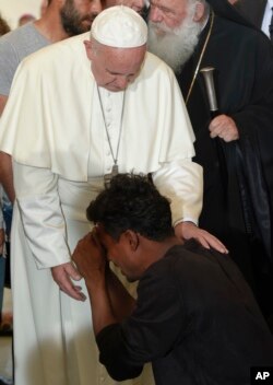 FILE - Pope Francis blesses a man kneeling in front of him, at the Moria refugee camp, on the Greek island of Lesbos, Saturday, April 16, 2016.