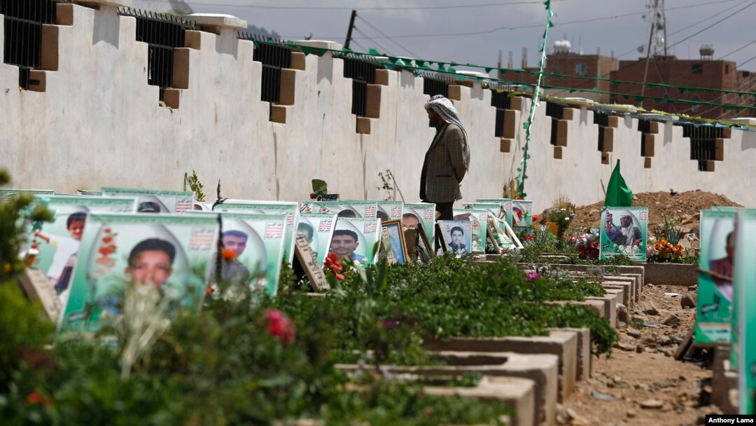 Seorang pemberontak Syiah Houthi berdiri di antara makam di Sana'a, Yaman, yang berhiaskan potret para pejuang dan pendukung Houthi yang tewas dalam konflik di Yaman (10/4). (AP/Hani Mohammed)