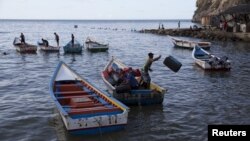 Men unload containers from a boat in the bay of Rio Caribe a town near Caribbean islands, in the eastern state of Sucre, Venezuela, Oct. 29, 2015. Authorities have reopened, Feb. 20, 2019, the country's maritime border with the Dutch Antilles islands a day after closing it.
