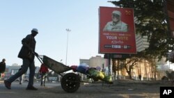 FILE - A man pushes a wheelbarrow past a billboard for Zambian presidential candidate Fred M'Membe in Lusaka, Zambia, July 5, 2021.