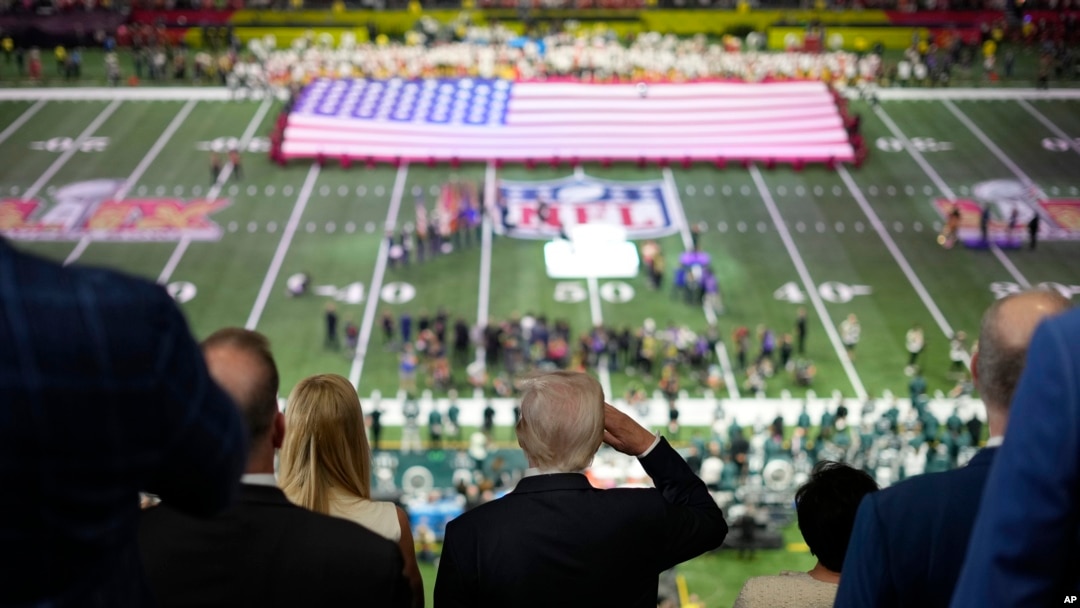 President Donald Trump, center, salutes as Jon Batiste performs the national anthem at the NFL Super Bowl 59 football game between the Philadelphia Eagles and the Kansas City Chiefs, in New Orleans, Louisiana, Feb. 9, 2025.