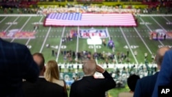 President Donald Trump, center, salutes as Jon Batiste performs the national anthem at the NFL Super Bowl 59 football game between the Philadelphia Eagles and the Kansas City Chiefs, in New Orleans, Louisiana, Feb. 9, 2025.