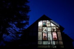 An image of veteran Alfred Healy is projected onto the home of his daughter, Eileen Driscoll, left, as she looks out the window with her sister, Patricia Creran, in Holyoke, Mass., May 7, 2020.