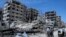 FILE - People stand in front of damaged buildings, in the town of Douma, the site of a suspected chemical weapons attack, near Damascus, Syria, April 16, 2018. 