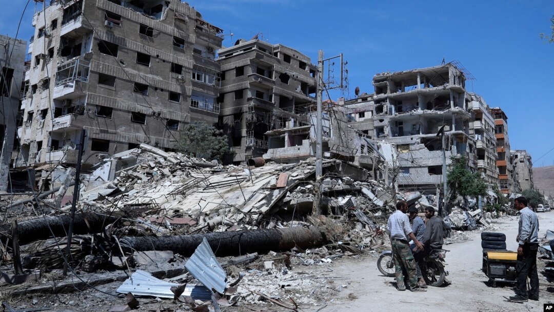 People stand in front of damaged buildings in the town of Douma, the site of a suspected chemical weapons attack, near Damascus, Syria, April 16, 2018. 