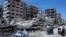People stand in front of damaged buildings in the town of Douma, the site of a suspected chemical weapons attack, near Damascus, Syria, April 16, 2018. 