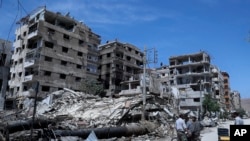 FILE - People stand in front of damaged buildings in the town of Douma, the site of a suspected chemical weapons attack, near Damascus, Syria, April 16, 2018. 