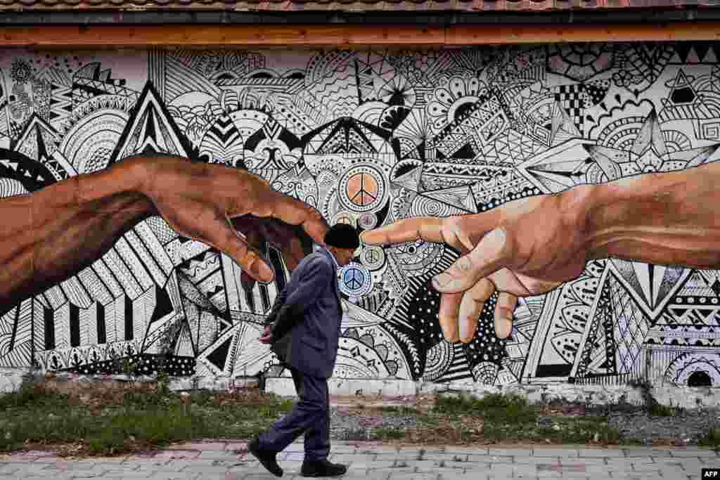 A pedestrian walks past a mural artwork painted on the wall of a house in the town of Ferizaj, Kosovo.
