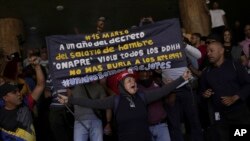 Un manifestante sostiene un cartel que exige mejores salarios mientras los partidarios del gobierno se paran detrás en un intento de que los manifestantes abandonen el Ministerio de Trabajo en Caracas, Venezuela, el miércoles 15 de marzo de 2023. (Foto AP/Matías Delacroix)