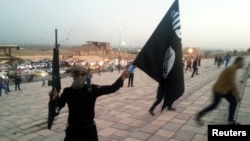 Seorang pejuang Negara Islam (ISIS) memegang bendera ISIS dan senjata di Mosul, Irak.