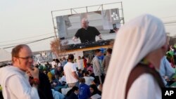 FILE - Roman Catholic priest Guilherme Peixoto, on video screen, plays techno music to help pilgrims wake up at Parque Tejo in Lisbon on Aug. 6, 2023, where Pope Francis will preside over a mass celebrating the 37th World Youth Day later in the day. (AP Photo/Ana Brigida)