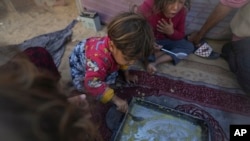 Girls in the Eid family eat lentils cooked by their mother, Yasmin, at their tent in a refugee camp in Deir al-Balah, Gaza Strip, Nov. 19, 2024. 