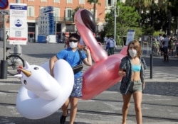 Tourists wearing face masks walk by a COVID-19 information sign in downtown Nice as France reinforces mask-wearing as a part of efforts to curb the resurgence of the coronavirus disease (COVID-19) across the country, in Nice, France August 11, 2020.