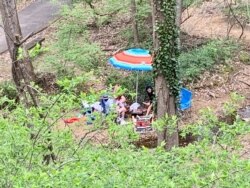 A family fired up a barbecue grill and sat on lounge chairs next to a creek to get a break from quarantine during COVID-19. (Carolyn Presutti/VOA)