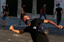 Anti-government protesters throw stones toward riot police during a protest marking the first anniversary of the massive blast at Beirut's port, near Parliament Square, in Beirut, Lebanon, Aug. 4, 2021.