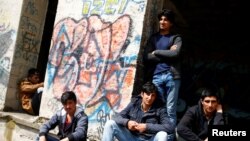 FILE - Migrants sit outside a dorm destroyed during the Bosnian 1992-1995 war, in Bihac, Bosnia and Herzegovina, May 11, 2018. 