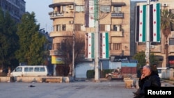 A man sits near flags placed by Syria's new leaders after the ousting of its longtime authoritarian President Bashar al-Assad, in Aleppo, Syria, Jan. 8, 2025.