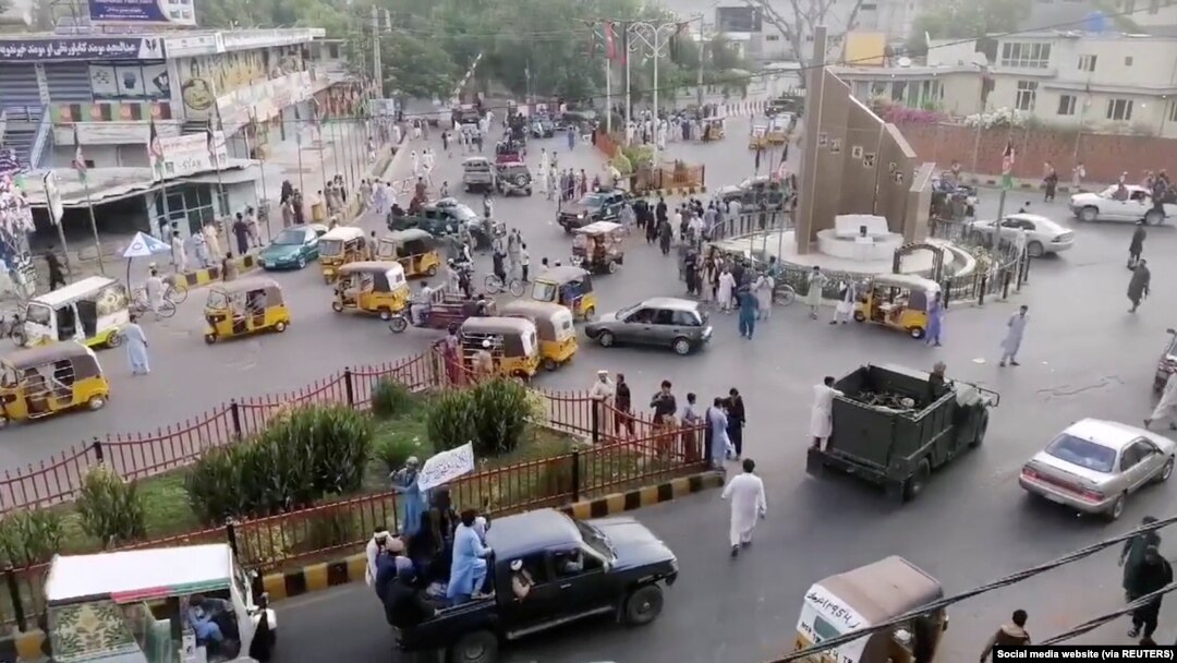 Taliban militants waving a Taliban flag on the back of a pickup truck drive past a crowded street at Pashtunistan Square area in Jalalabad, Afghanistan in this still image taken from social media video uploaded on August 15, 2021. Social media website/via REUTERS THIS IMAGE HAS B