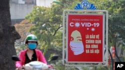 A motorcyclist drives past a poster calling people to take care of their health against the new coronavirus in Hanoi, Vietnam Tuesday, April 14, 2020. The new coronavirus causes mild or moderate symptoms for most people, but for some, especially…