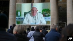 People look at a giant screen in St.Peter's Square, at the Vatican, showing Pope Francis reciting the Angelus noon prayer from his residence, after he decided not to appear at the window of his studio because of a persistent cold, Dec. 22, 2024.