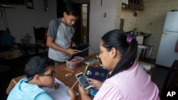 Leidy Martínez lee la tarea de su hijo en su teléfono celular, mientras su otro hijo Joandry, de 12 años, verifica la conexión a internet en una tableta en su casa en el barrio de Las Mayas en Caracas, el jueves 7 de mayo de 2020.