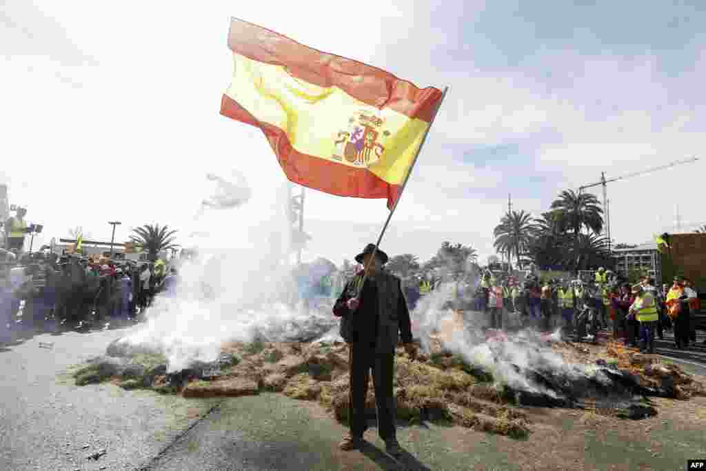 A protester waves a Spanish flag as hay burns during a farmers protest to denounce their conditions and the European agricultural policy, aiming to block the port of Valencia.