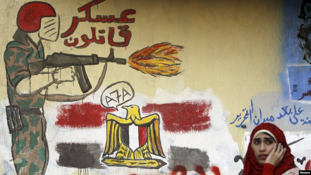 A woman sits in front of a wall filled with graffiti against the Supreme Council of the Armed Forces near Tahrir Square in Cairo, June 5, 2012.