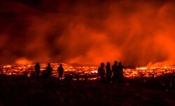 People watch as lava flows from an eruption of a volcano on the Reykjanes Peninsula in southwestern Iceland late on March 24, 2021.
