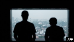 This photo taken on October 15, 2024 shows two Indonesian men, who previously fell victims of human trafficking syndicates and were forced to work as scammers in Cambodia, posing at a window as they speak to AFP in Jakarta.