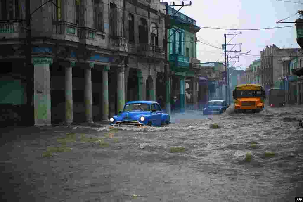 Old American cars and buses drive through a flooded street in Havana, Cuba, June 30, 2021.