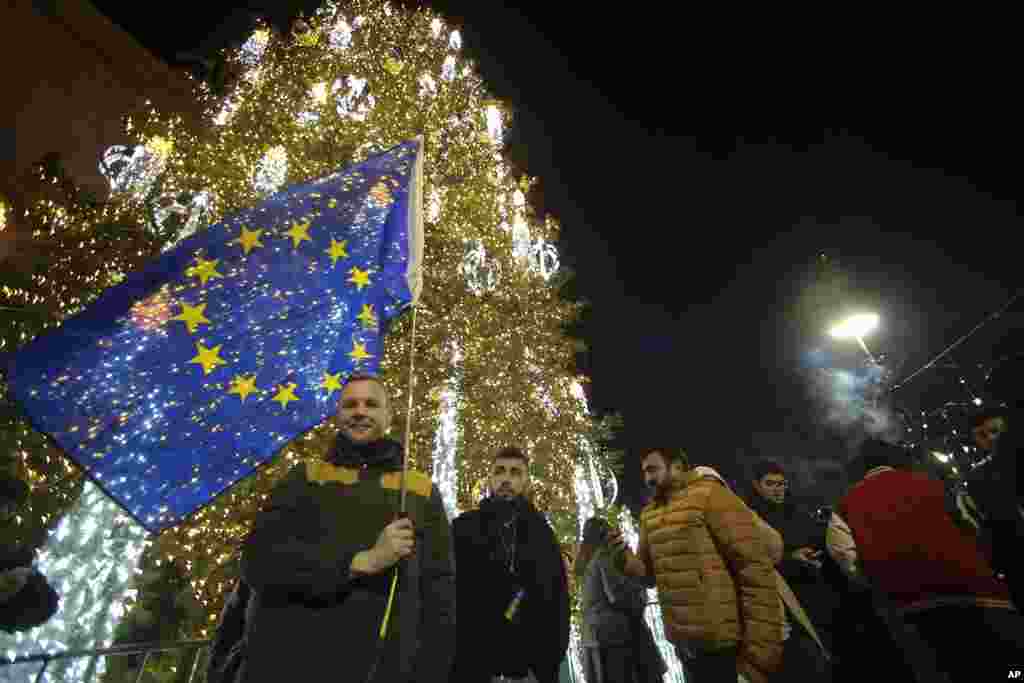 A man with an EU flag stands next to a Christmas tree in a street decorated for Christmas and the New Year festivities celebrating on New Year outside of the Georgian parliament, in Tbilisi, Georgia, Jan. 1, 2025.